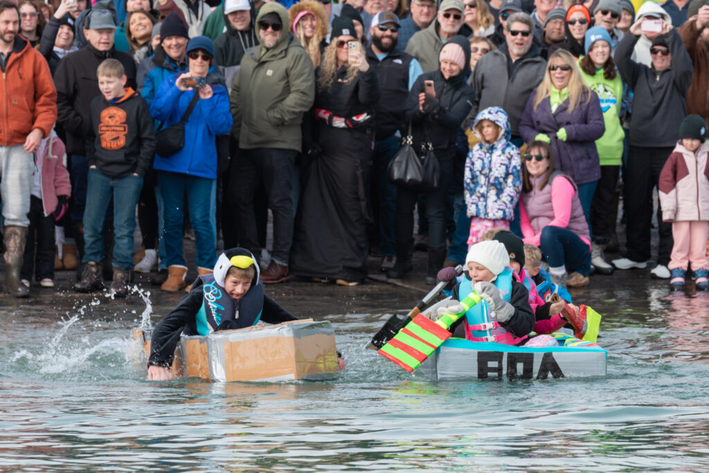 Two children in costumes trying to paddle home made boats made from cardboard.